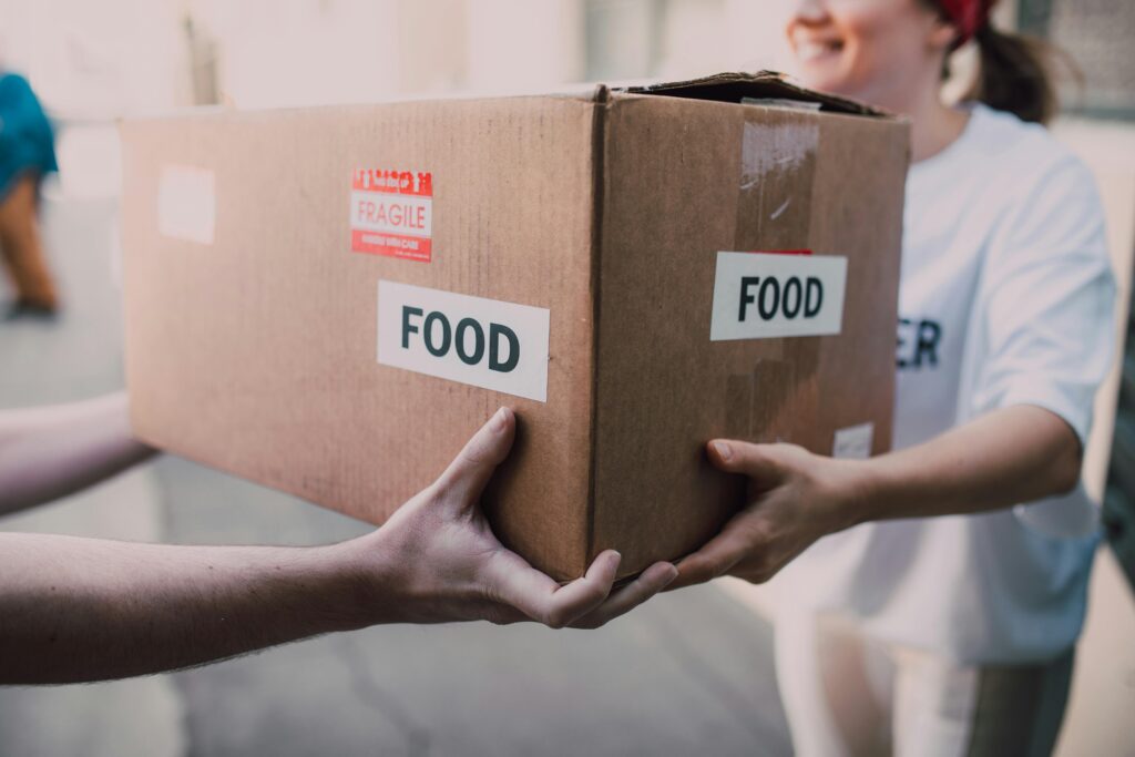 Hands exchanging a box labeled 'Food', symbolizing charity and support.